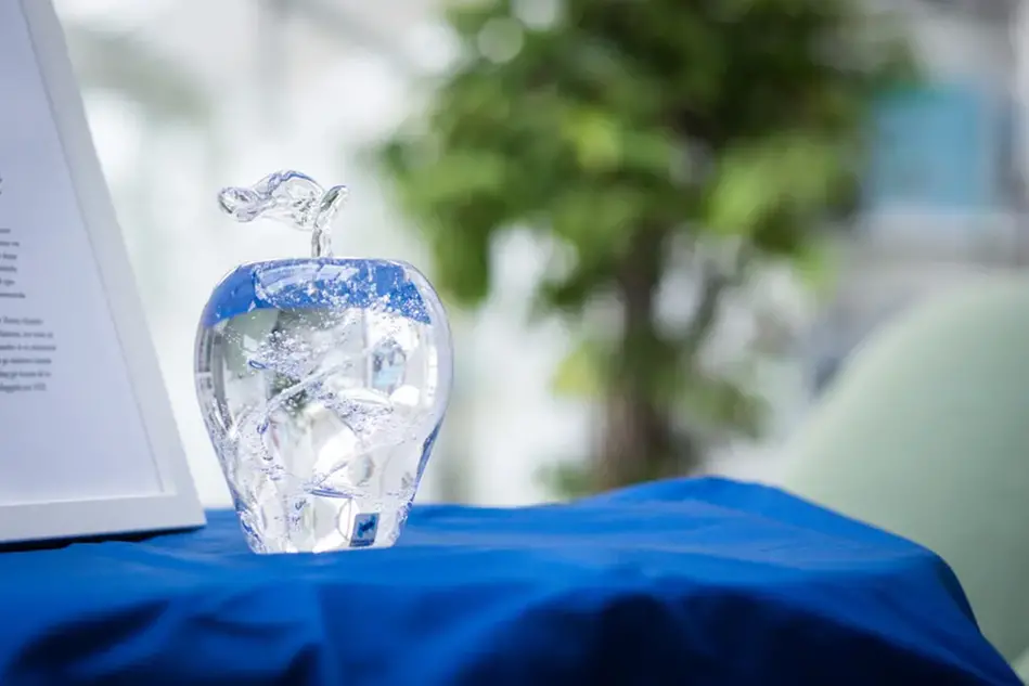 A glass apple on a table next to a framed diploma.