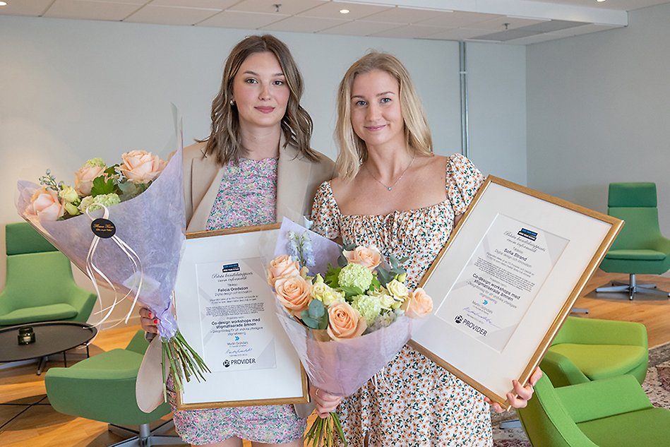 Två kvinnor står med diplom och blommor. Foto.