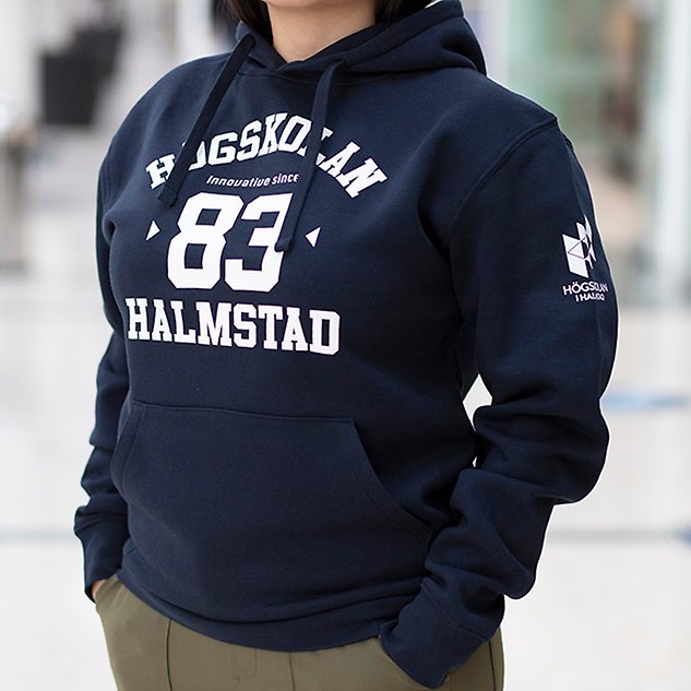 A dark blue long-sleeved shirt with the text "Högskolan 83 Halmstad" in white text is shown on a person whose upper body is visible in the picture. Photo.