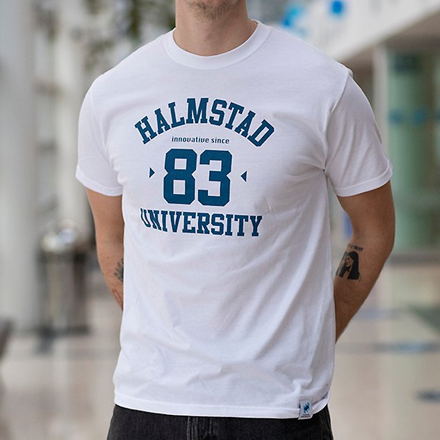 En vit t-shirt med texten ”Halmstad 83 University” i blå text sitter på en person vars överkropp syns i bild. Foto.