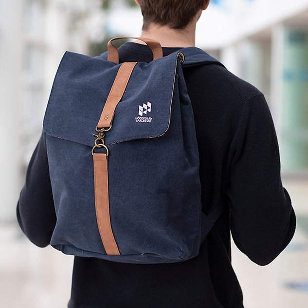 A person, seen from behind, carries a blue backpack. Photo.