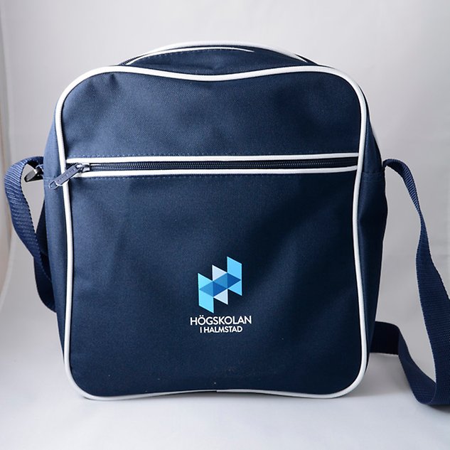 A dark blue shoulder bag with the Halmstad University logo seen from the front. Photo.