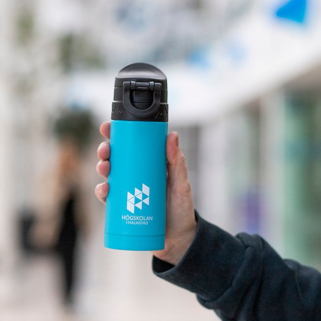 A hand holds up a turquoise thermos with a white logo on it. Photo.