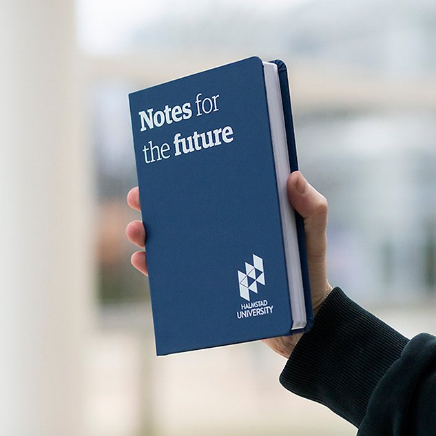 A hand holds up a dark blue notebook with the text ”Notes for the future” in English. Photo.