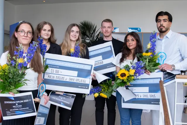Sex studenter håller i en varsin stor check och blommor och ler mot kameran. Foto.