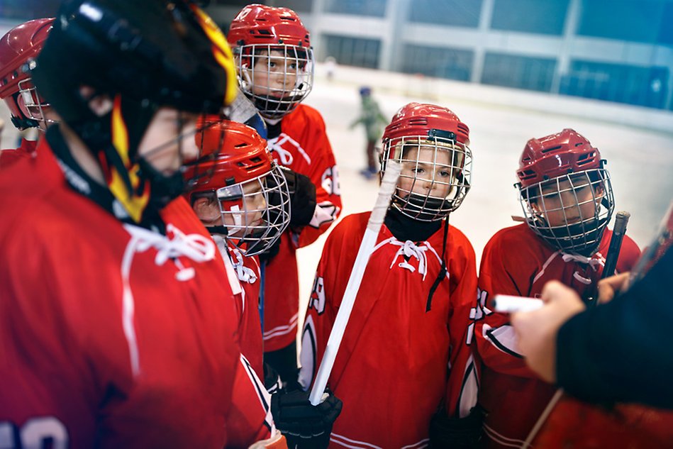 A few very young ice hockey players gathered around their coach giving instructions. Photo.