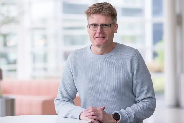 Person in grey jumper with glasses smiling at camera.