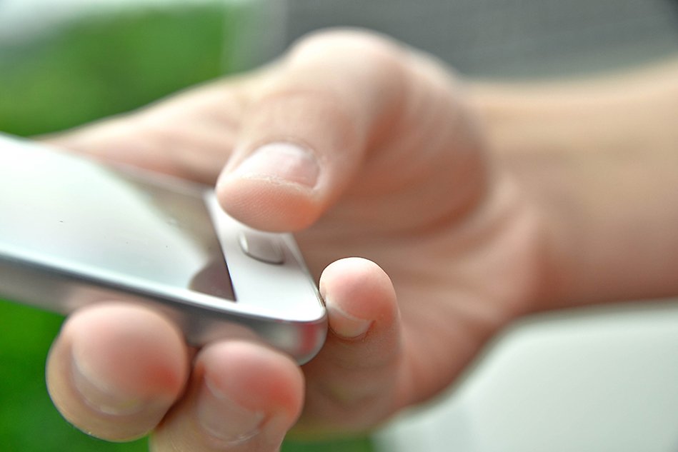 Hand holding a smartphone, the thumb held over the home button.