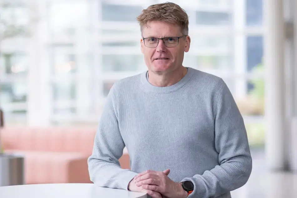 Person in grey jumper with glasses smiling at camera.