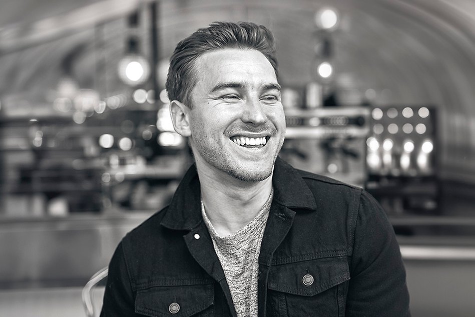 En man sitter på ett kafé iklädd jeansjacka och skrattar. Svartvit bild.