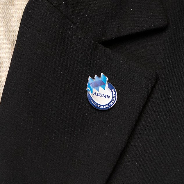 A pin with a logo and the text ”Alumni” in Swedish is seen on a blazer lapel. Photo.