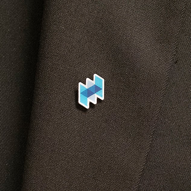 A pin in the shape of joined triangles is seen on a blazer lapel. Photo.
