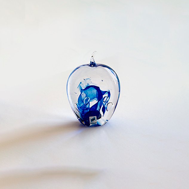 Glass art in the shape of an apple with a blue pattern inside. Photo.