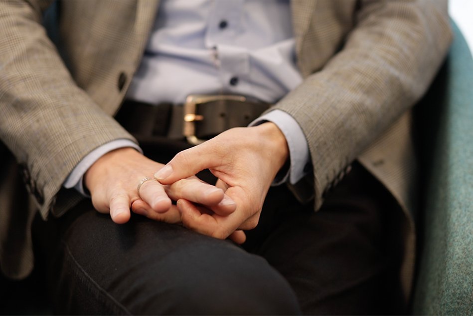 Close-up of a person’s hands in their lap. One hand is touching a ring on the other hand.