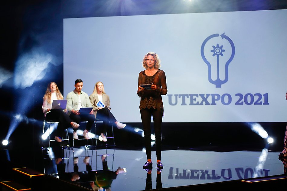 Kvinna står på scen med texten Utexpo 2021 bakom sig. På scenen sitter också tre personer på höga stolar. 
