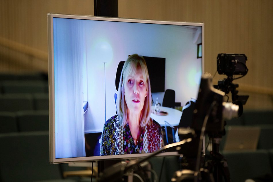 A big screen showing a woman talking. A camera is in the foreground. Photo.