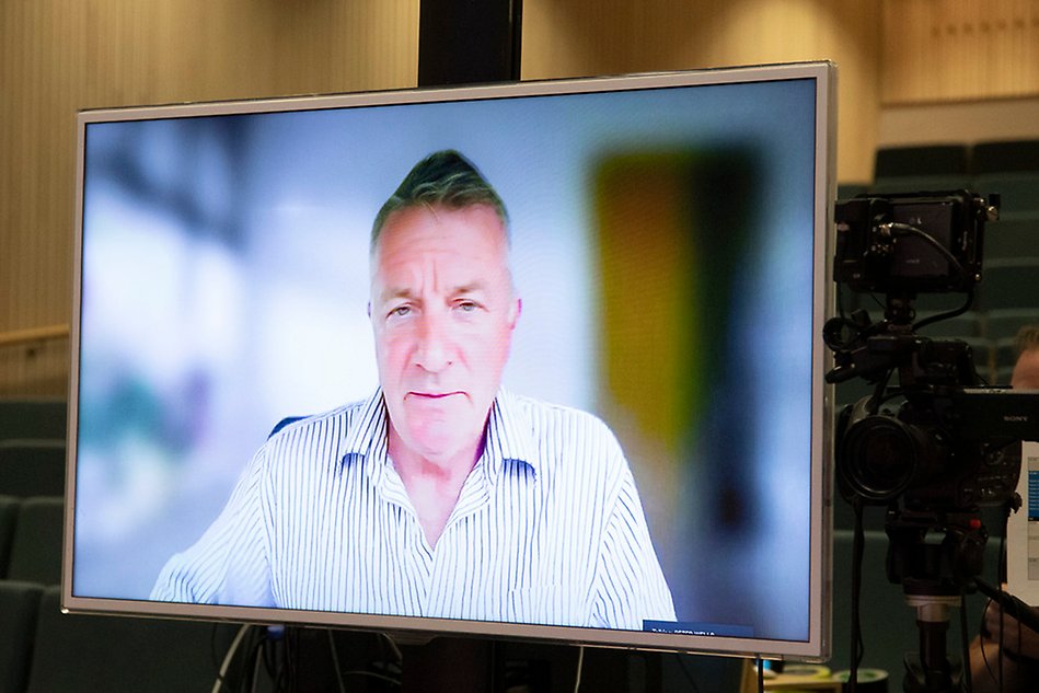 A big screen showing a man in a stripey shirt. A camera screen is in the foreground. Photo.