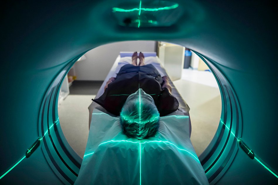 Person liggande på en bår väg in i en röntgenmaskin med grönt ljus. Foto.