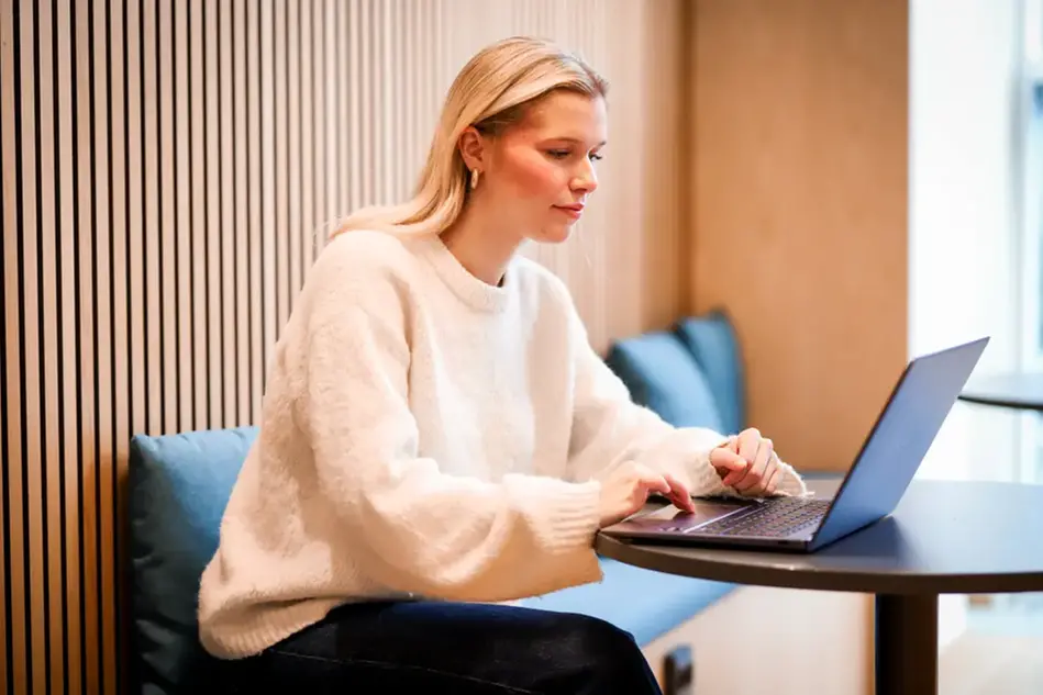 En ung person sitter vid ett bord och arbetar på en laptop.