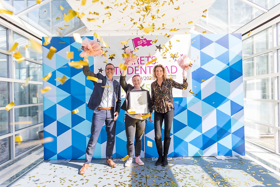 Tre personer i konfettiregn framför en banderoll med texten Årets studentstad. Foto.