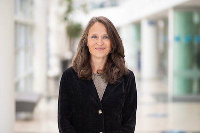 Woman with long hair and dark jacket looks into the camera. Photo