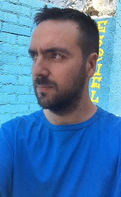 A man in a blue t-shirt stands in half-profile looking away from the camera.